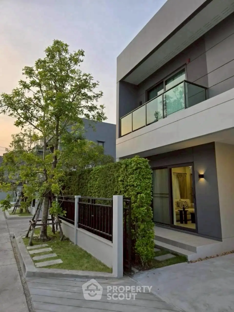 Modern two-story house with balcony and lush greenery in a serene neighborhood.