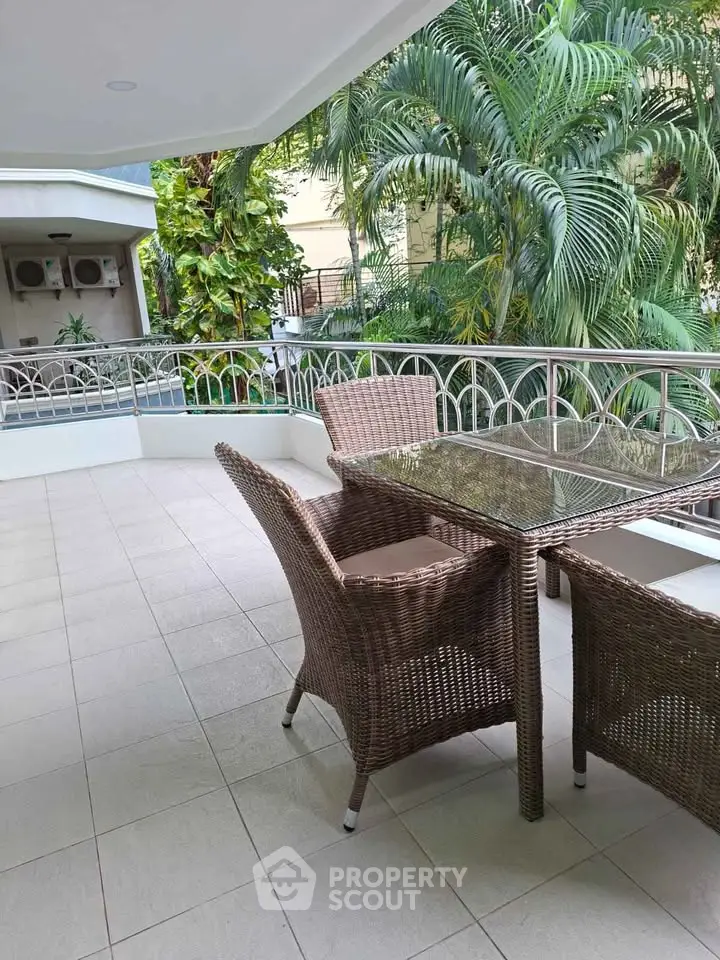 Spacious balcony with elegant wicker furniture and lush greenery view, perfect for outdoor relaxation.