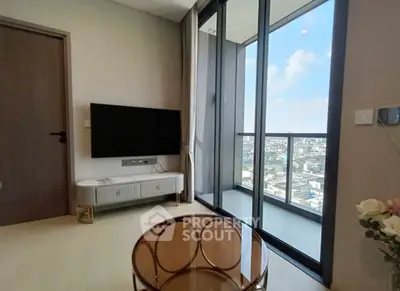Modern living room with balcony and city view, featuring sleek furniture and large glass doors.