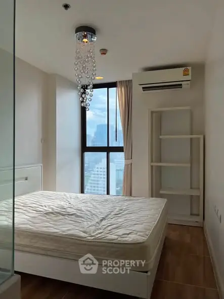 Modern bedroom with large window and city view, featuring a stylish chandelier and air conditioning.