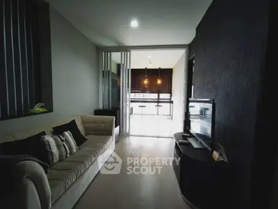 Modern living room with cozy sofa and sleek TV setup leading to a bright kitchen area.