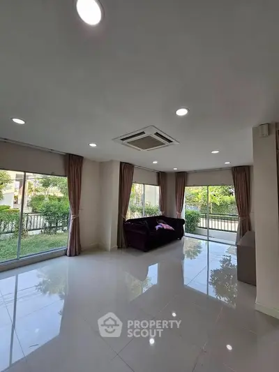 Spacious living room with large windows and garden view, featuring modern ceiling lights and elegant curtains.