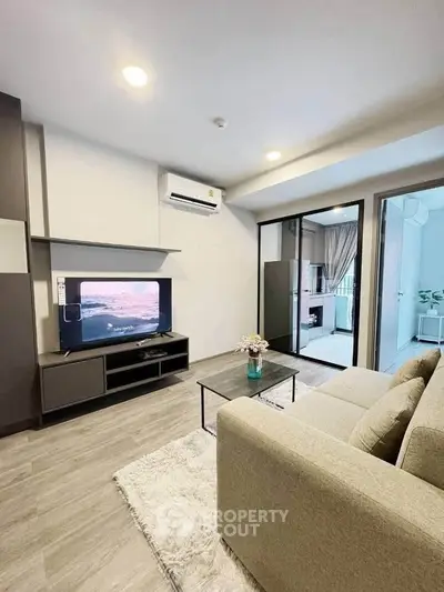 Modern living room with cozy sofa, TV, and sliding glass doors leading to a bright bedroom.