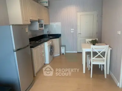 Modern kitchen with dining area, featuring appliances like fridge and washing machine, in a cozy apartment setting.