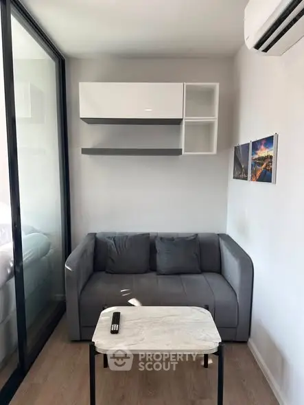 Modern living room with sleek gray sofa, wall-mounted shelves, and air conditioning, perfect for urban living.