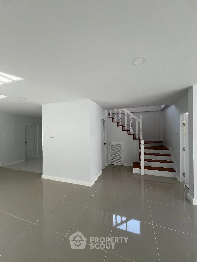 Spacious and bright open-plan living area with glossy tiled flooring and a striking red staircase leading to the upper level, perfect for modern living.