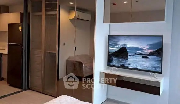 Modern studio apartment with sleek design, featuring a wall-mounted TV and compact kitchen area.