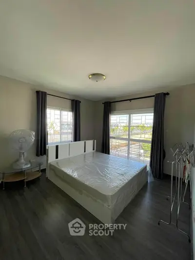 Spacious bedroom with large windows allowing ample natural light, featuring elegant dark curtains and a sleek modern bed frame, set on beautiful laminate flooring.