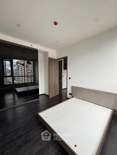 Modern bedroom with dark wood flooring and mirrored closet in urban apartment
