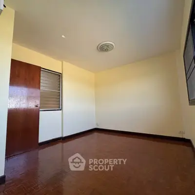 Spacious empty room with wooden flooring and large window, ideal for customization.