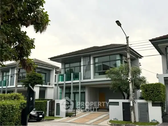 Modern two-story house with large windows and landscaped front yard in a suburban neighborhood.