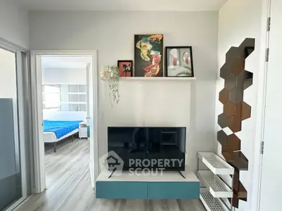 Modern living room with stylish decor and view into a cozy bedroom, featuring a sleek TV setup and artistic wall accents.