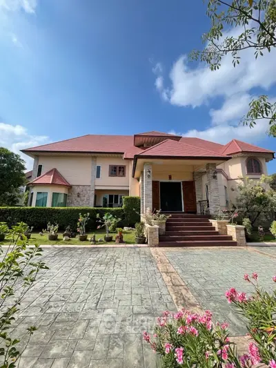 Stunning two-story house with red roof, lush garden, and spacious driveway under a clear blue sky.