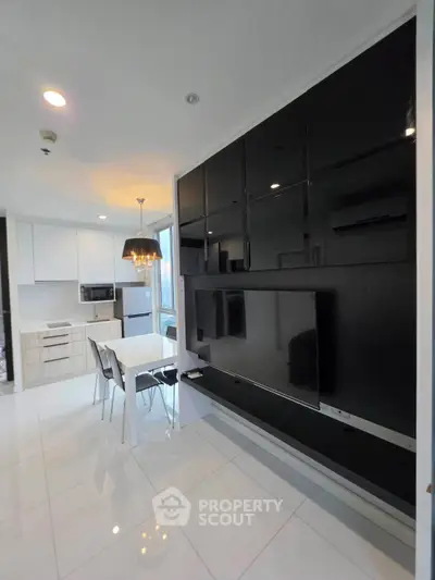 Modern open-plan living room with sleek black entertainment unit and dining area, featuring contemporary lighting.