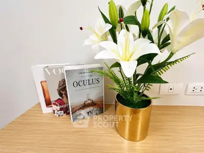 Elegant interior decor with stylish magazines and a gold vase with white lilies on a wooden table.