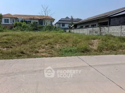 Vacant land plot in suburban neighborhood with nearby houses and clear sky.