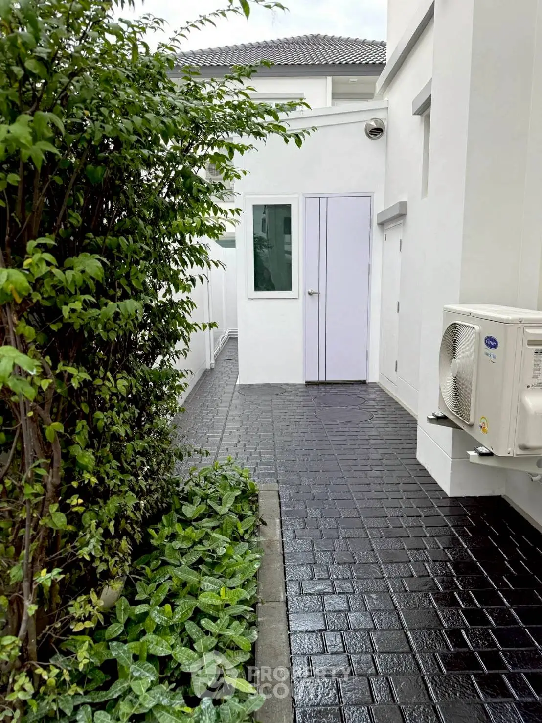 Modern exterior view of a white house with lush greenery and sleek air conditioning unit.