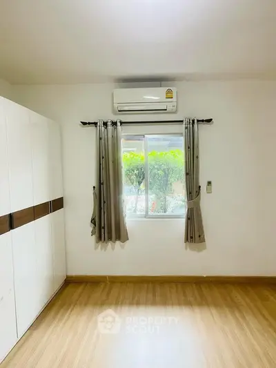 Bright bedroom with air conditioning and large window overlooking greenery.
