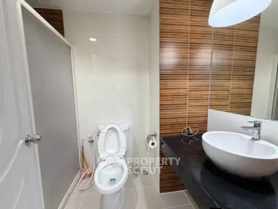 Modern bathroom with sleek design featuring a vessel sink and wood accent wall.
