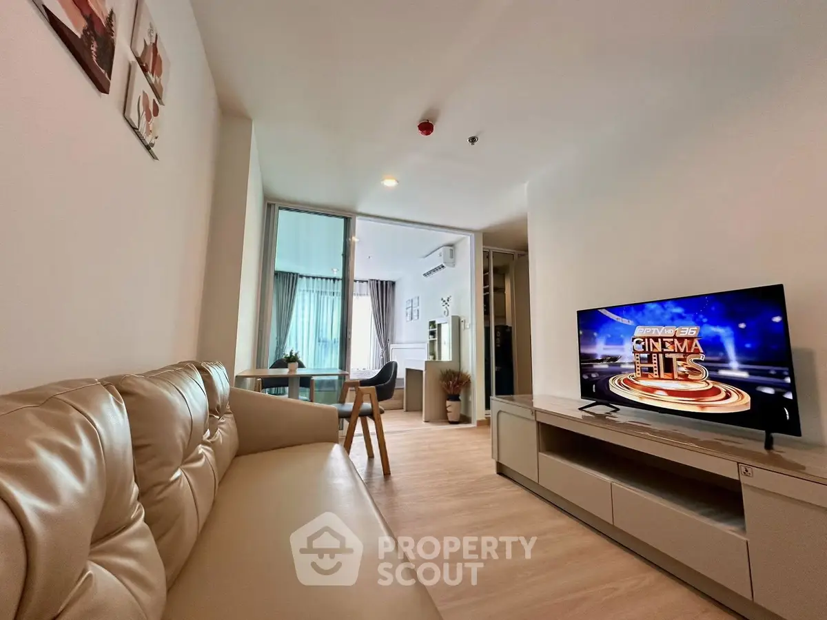 Modern living room with cozy sofa and TV, open layout leading to dining area with natural light.