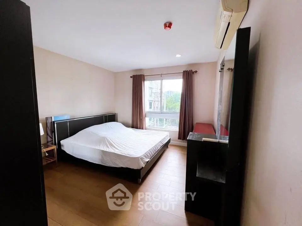 Spacious bedroom with large window and wooden flooring in modern apartment.