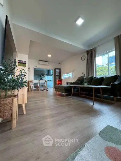 Spacious living room with modern decor and open kitchen layout, featuring large windows and stylish furniture.