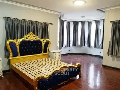 Luxurious bedroom with ornate bed frame and elegant curtains, showcasing rich wooden flooring.