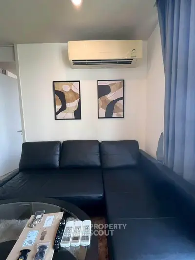 Modern living room with black leather sofa and wall art, featuring air conditioning for comfort.