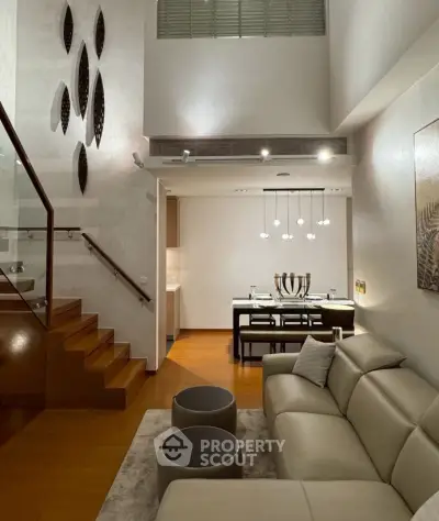 Modern living room with elegant staircase and dining area, featuring stylish lighting and contemporary decor.