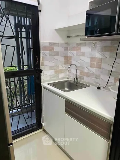 Compact modern kitchen with sleek cabinetry and tiled backsplash, featuring a built-in microwave and stainless steel sink.