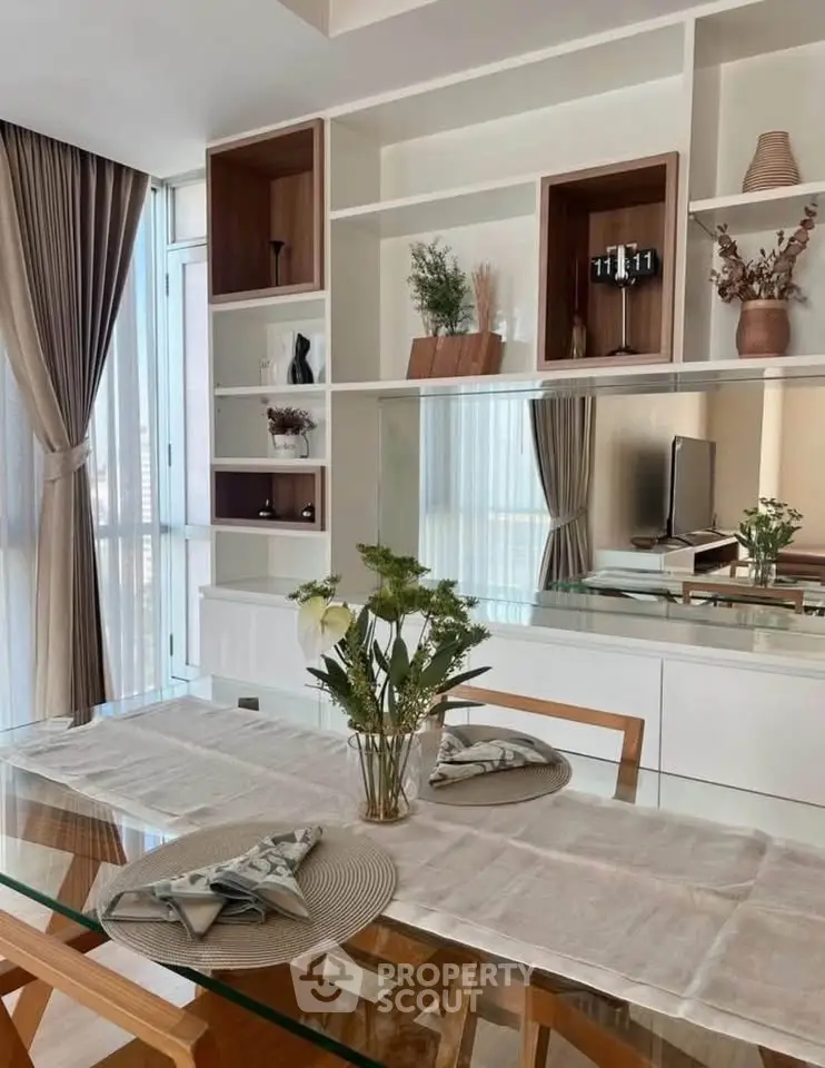 Elegant dining area with glass table, stylish shelving, and natural light in modern apartment.