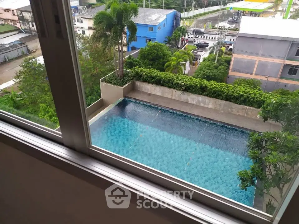 Stunning pool view from high-rise apartment window, lush greenery surrounds modern swimming area.