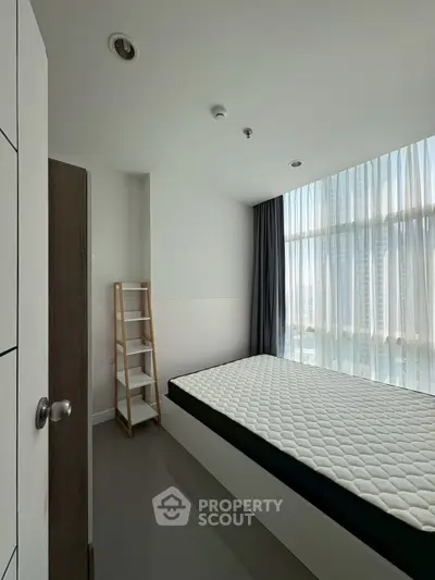 Modern minimalist bedroom with large window and natural light in urban apartment.