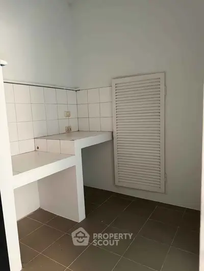 Compact utility room with tiled countertop and louvered door, ideal for storage or laundry setup.