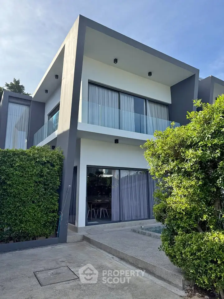 Modern two-story house with large windows and lush greenery, showcasing contemporary architecture and inviting outdoor space.