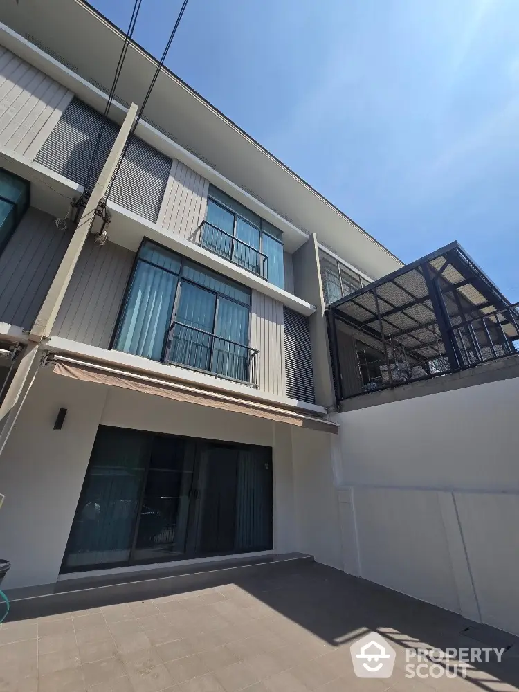 Modern three-story townhouse with large windows and balcony under clear blue sky