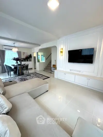 Elegant living room with modern decor and open dining area, featuring a wall-mounted TV and stylish furniture.