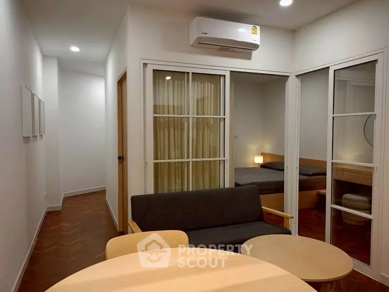 Modern apartment interior with cozy living room and bedroom, featuring sleek furniture and air conditioning.
