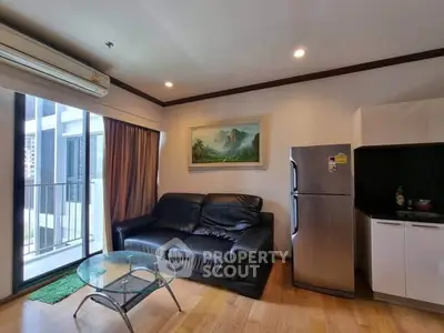 Modern living room with balcony, leather sofa, glass coffee table, and stainless steel fridge in a cozy apartment.