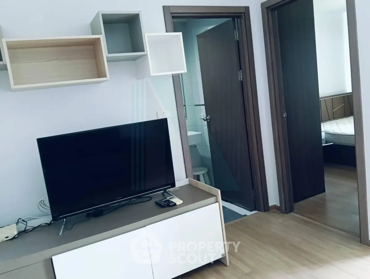 Modern living room with TV and open view to bedroom and bathroom, showcasing sleek design and functionality.