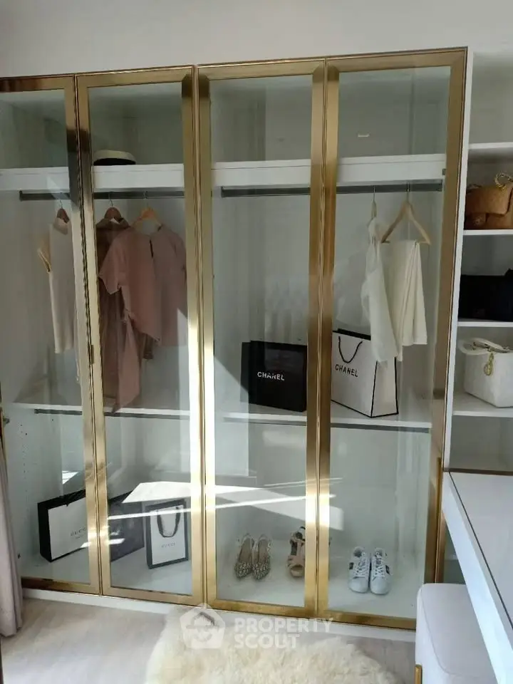 Luxurious walk-in closet with gold-framed glass doors and designer items on display.