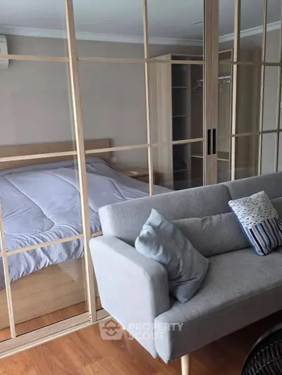 Modern bedroom with glass partition and cozy living area, featuring stylish furniture and wooden flooring.