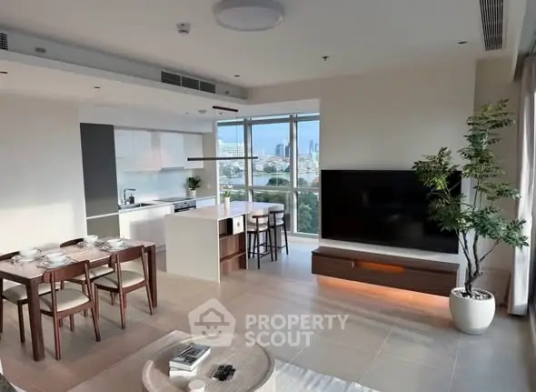 Modern open-plan living room with kitchen, large TV, and city view from windows.