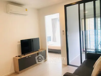 Modern living room with TV and air conditioning, leading to a cozy bedroom through sliding glass doors.