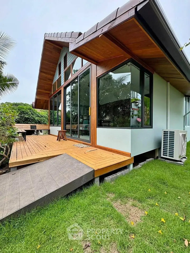 Modern home with large windows and wooden deck surrounded by lush greenery