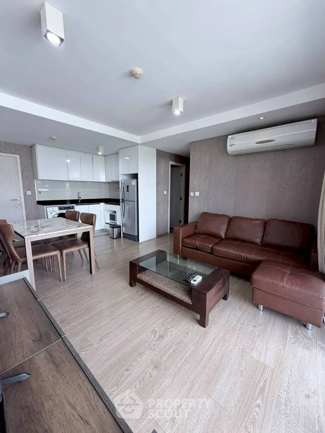 Modern living room with open kitchen, featuring sleek furniture and air conditioning.