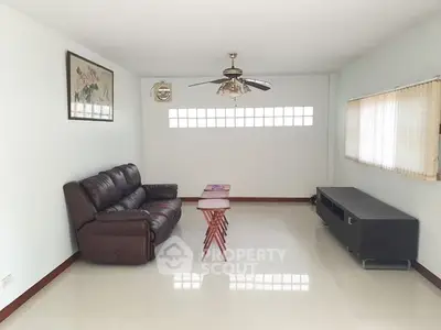 Spacious living room with leather sofa and ceiling fan, perfect for relaxation.