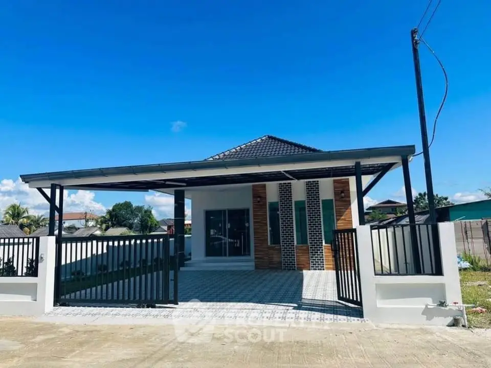 Modern single-story house with spacious driveway and sleek metal gate under clear blue sky.
