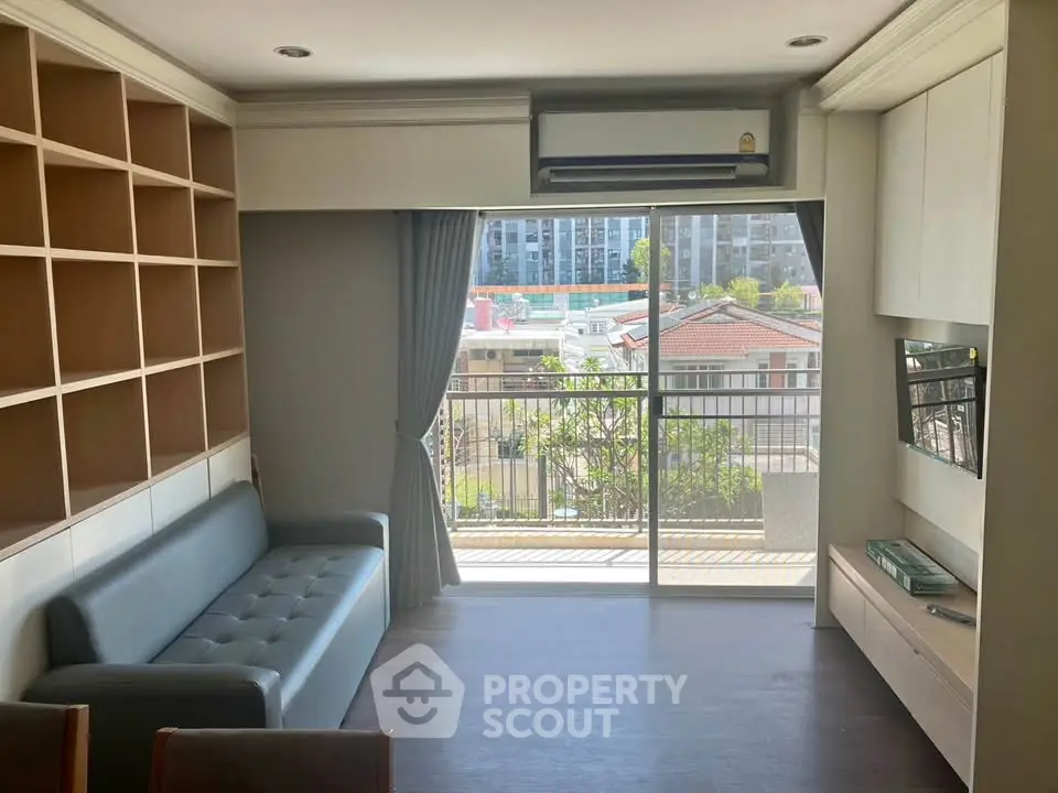 Modern living room with balcony view, featuring sleek furniture and built-in shelving.