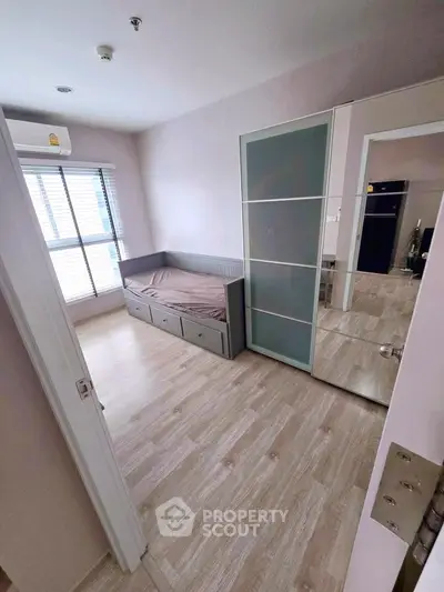 Cozy bedroom with wooden flooring, large window, and modern furniture in a bright apartment.